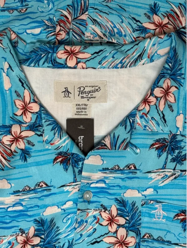 Men's Penguin Tropical Rayon Shirt, a blue short-sleeve button-down with a print of tropical flowers, palm trees, and sailboats.
