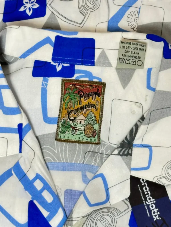 Pineapple Connection Rayon Shirt - Men's short-sleeve button-down with an abstract print of blue squares, gray shapes, and stylized tiki masks and surfboards on a white background.