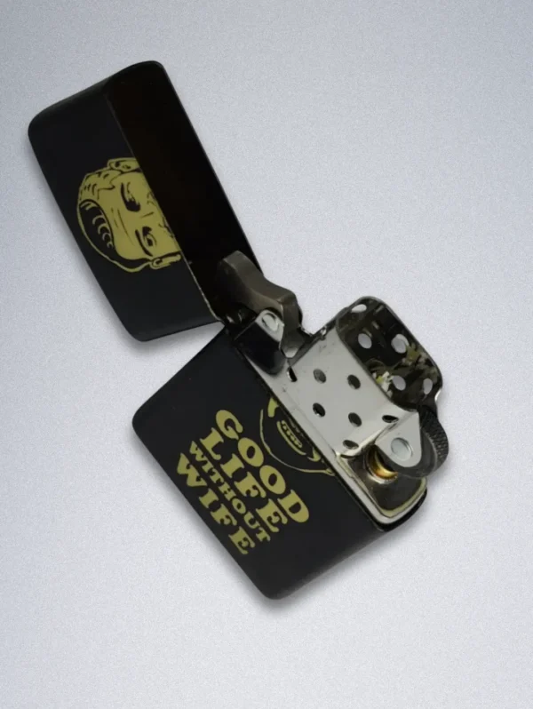 A matte black Zippo lighter with a gold graphic of a smiling, bearded man and the text "GOOD LIFE WITHOUT WIFE".